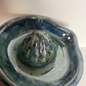 Puede incluir: Un exprimidor de cítricos de cerámica azul y blanco con un centro texturizado y elevado. El exprimidor tiene un asa y un pequeño pico para verter.