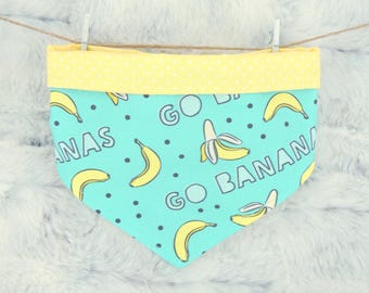 May include: A turquoise dog bandana with a yellow polka dot trim. The bandana features yellow bananas and the words "GO BANANAS" in a playful font. The bandana is hanging from a clothesline.