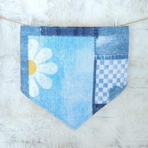 Peut inclure: Un bandana pour animaux de compagnie à motifs bleus et blancs avec un motif de marguerite. Le bandana est fait de tissu et est suspendu à une corde à linge. Le bandana a un motif patchwork avec une marguerite, du vichy et du denim.
