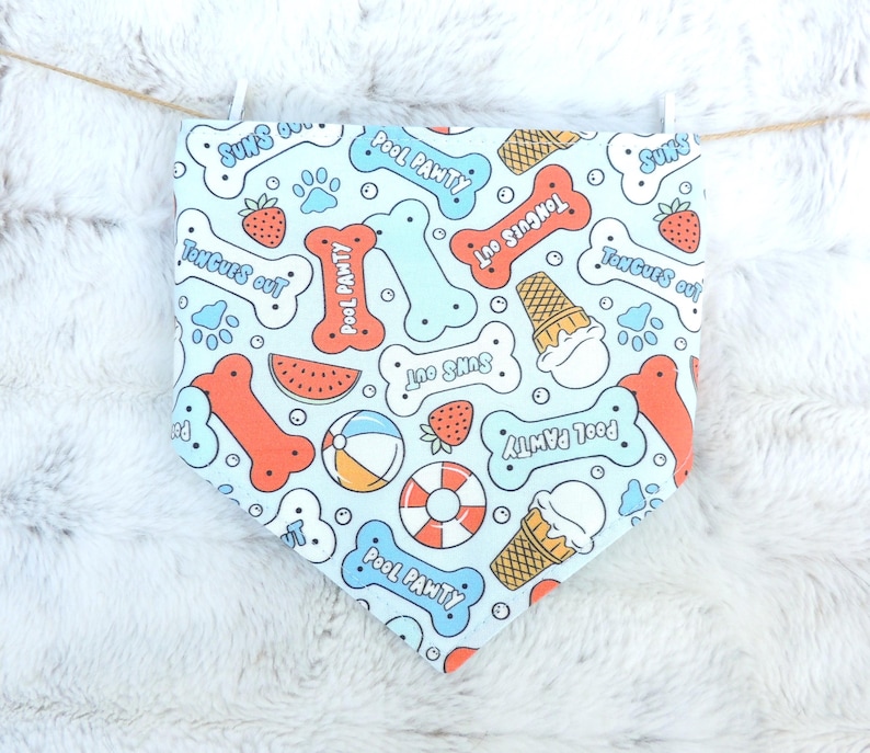 May include: A light blue dog bandana with a repeating pattern of bones, ice cream cones, strawberries, and beach balls. The bandana has the phrases "Pool Pawty", "Tongues Out", and "Sun's Out" printed on it.