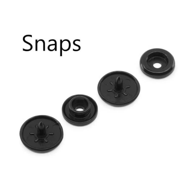 May include: Black snap fasteners in various sizes are arranged on a white background. The word "Snaps" is printed in black, above the fasteners. These fasteners are commonly used in clothing and accessories.