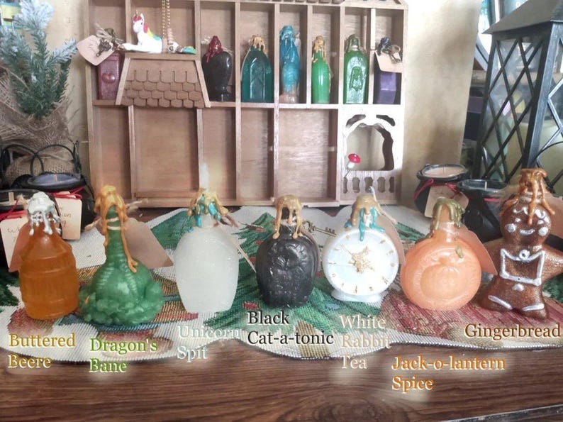 May include: Assortment of small glass bottles with various colored liquids and decorative stoppers. The bottles are labeled with names like "Buttered Beere", "Dragon's Bane", "Unicorn Spit", "Black Cat-a-tonic", "White Rabbit Tea", "Jack-o-lantern Spice", and "Gingerbread".