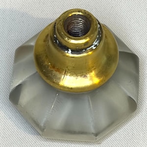 May include: A cabinet knob featuring a frosted, translucent, octagonal glass base with a faceted surface. The center of the knob is fitted with a metallic, gold-toned brass mounting post that includes a threaded interior hole for attachment.