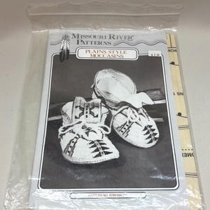May include: A sewing pattern envelope titled Missouri River Patterns Plains Style Moccasins, featuring a black and white illustration of two beaded moccasins with geometric designs, enclosed in a clear plastic bag with pattern number 4799-500.