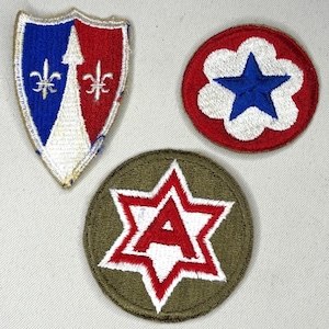May include: Three embroidered fabric patches. One shield-shaped patch features a blue and red background with a white central arrow and two fleur-de-lis. A circular red patch displays a white cloud shape with a blue star. A circular olive green patch shows a white six-pointed star with a red letter A.