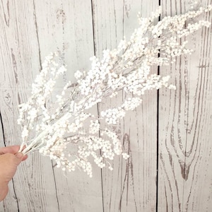 May include: A white spray of faux berries with a silvery sheen, perfect for adding a touch of wintery elegance to your home decor.