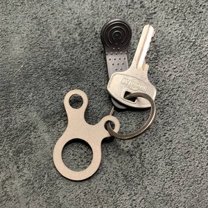 May include: A silver key ring with a small, round, metal loop and two prongs. The key ring is attached to a silver key with a black rubber key cover and the text "IMPERIAL" on the key.