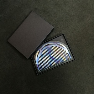 May include: A rainbow-colored metal comb with a curved design, in a black leather case.