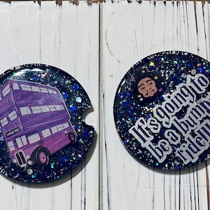 May include: Two round, black and blue glitter coasters. One coaster features a purple double-decker bus with the text "Knight Bus". The other coaster features a cartoon character with the text "It's going to be a bumpy ride!!"