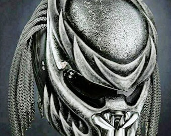 May include: A detailed, metallic Predator helmet with intricate designs and a textured surface. The helmet features a silver and black color scheme, with chain-like details on the sides and a distinctive jaw structure. The overall design is highly detailed and futuristic.