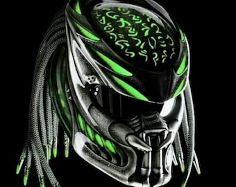 Può includere: Un casco da moto futuristico con un design da predatore. Il casco presenta una combinazione di colori nero e argento con accenti verde neon. Il design include un volto dettagliato, dreadlocks e un motivo intricato sulla parte superiore.