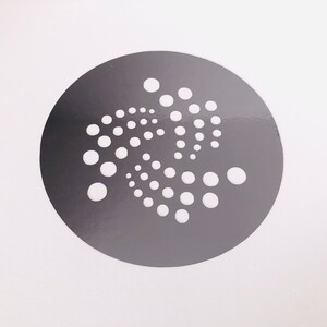 Pu&ograve; includere: Un adesivo circolare grigio con un design stilizzato bianco di un motivo a punti a spirale.