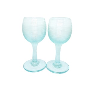 May include: Two clear blue glass shot glasses with a textured, rippled design. The glasses have a round base and a tall, slender stem.