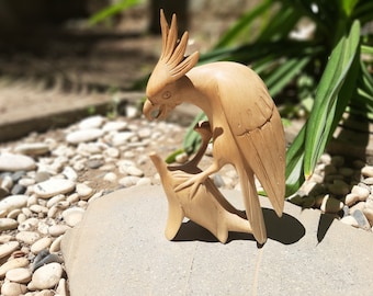 May include: A wooden carving of a parrot perched on a smaller bird. The parrot is light brown and has a long, pointed beak. The smaller bird is also light brown and has a short, rounded beak.