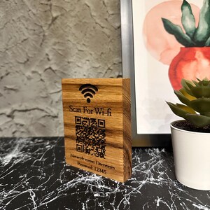 Peut inclure: Un panneau Wi-Fi en bois avec le texte "Scan For Wi-fi", un code QR et des informations sur le réseau. Le panneau est en bois brun clair et comporte un symbole Wi-Fi en haut. Le nom du réseau est Decorium et le mot de passe est 12345.