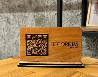May include: A wooden sign with a black base and a QR code and the text "DECORIUM WOOD" engraved on it.