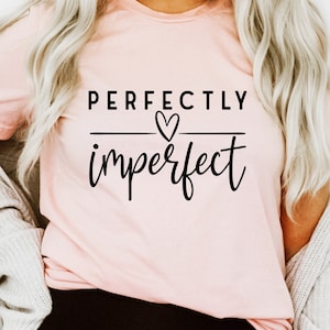 May include: A pink t-shirt with the text "PERFECTLY imperfect" in black lettering with a small heart symbol above the word "imperfect".