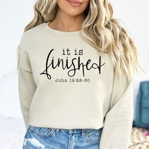 May include: A beige sweatshirt with the text "it is finished" in black cursive lettering and the scripture reference "John 19:28-30" below.