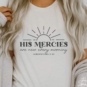 Puede incluir: Camiseta blanca con un diseño gráfico negro de un sol con rayos y el texto "HIS MERCIES are new every morning" con la referencia bíblica "LAMENTATIONS 3:23".