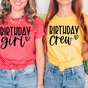 May include: Two people wearing matching t-shirts. The person on the left is wearing a red shirt with the text "Birthday girl" in black. The person on the right is wearing a yellow shirt with the text "Birthday Crew" in black.