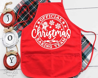May include: Red Christmas baking apron with a white circle design that says "Official Christmas Baking Team" with a gingerbread man, snowflakes, and a rolling pin inside the circle.