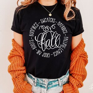 May include: Black t-shirt with a white graphic of a pumpkin and the word "fall" surrounded by text that reads "Crisp Air - Boots - Bonfires - Sweaters - Hayrides - Falling Leaves".