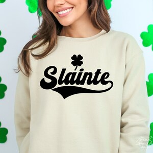 May include: A beige sweatshirt with a black shamrock and the word "Slainte" in a black retro font.