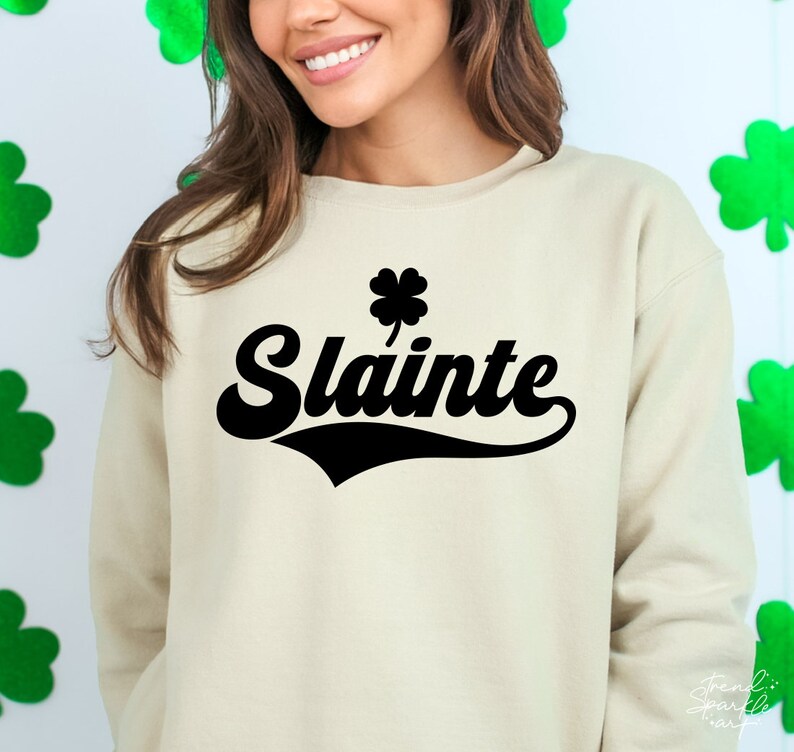 May include: A beige sweatshirt with a black shamrock and the word "Slainte" in a black retro font.