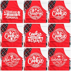 May include: Red aprons with white text and designs. The aprons feature phrases like "Baking Christmas Memories," "Official Christmas Baking Team," and "Proud Member of the Cookie Baking Crew." Other aprons say "Cookie Taster," "Cookie Baking Crew," and "Cookie Decorating Crew."