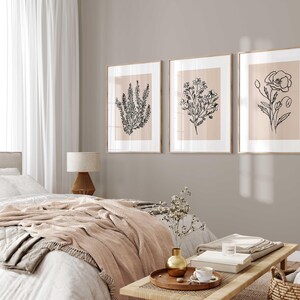 Puede incluir: Tres impresiones enmarcadas de dibujos en blanco y negro de flores sobre un fondo beige claro. Las impresiones est&aacute;n colgadas en una pared gris claro en un dormitorio.