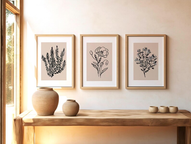 Puede incluir: Tres impresiones enmarcadas con dibujos de l&iacute;nea negra de diferentes flores sobre un fondo beige claro. Los marcos son de madera clara y est&aacute;n colgados en una pared blanca.