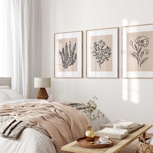 Puede incluir: Tres dibujos en blanco y negro de plantas enmarcados sobre un fondo rosa claro. Los dibujos son de una amapola, un grupo de flores peque&ntilde;as y una rama de lavanda. Los marcos son de madera clara y est&aacute;n colgados en una pared blanca.