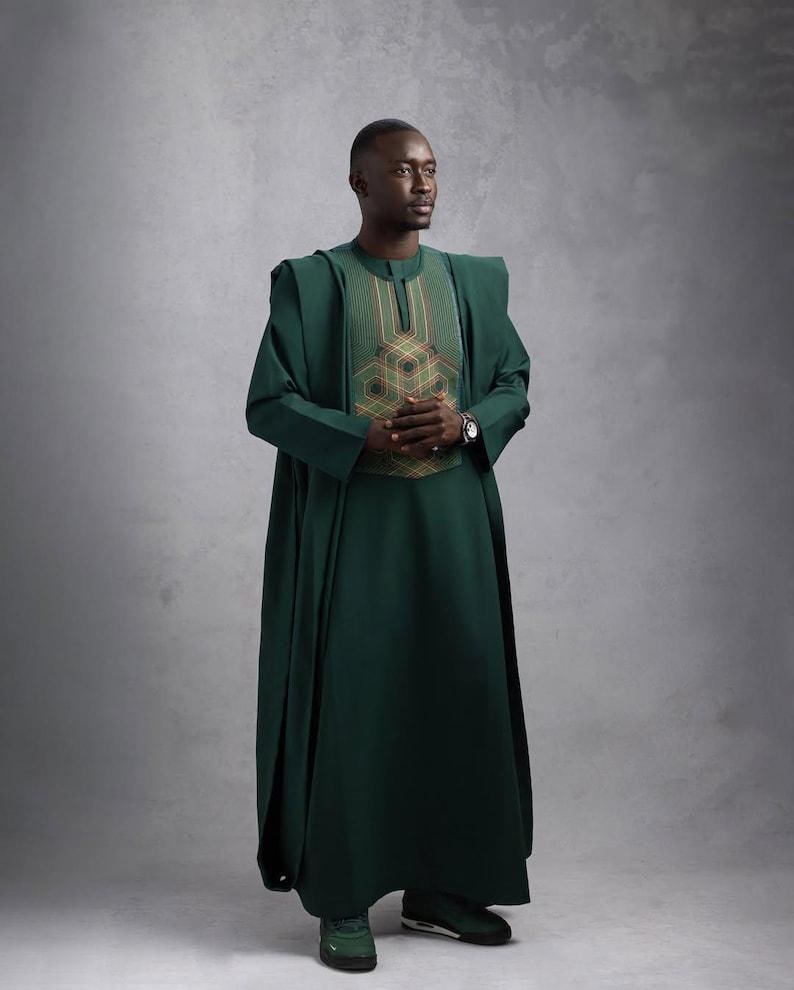 May include: A dark green traditional outfit with intricate embroidery on the chest. The outfit includes a long, flowing robe and matching pants. The person is wearing a watch and dark green sneakers.