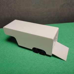 Può includere: Rimorchio giocattolo bianco con una rampa e ruote nere. Il rimorchio è in plastica e ha un design semplice.