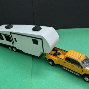 May include: A yellow pickup truck towing a white and black camper trailer. The camper has multiple windows and black accents. The truck has a detailed design with black wheels.