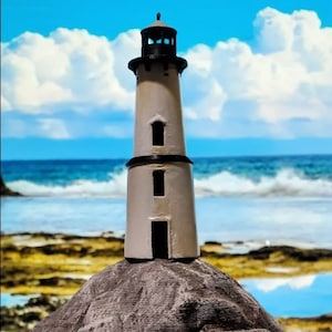 May include: A white lighthouse model with a black roof and windows, standing on a gray rock against a blue sky with white clouds and a blue ocean in the background.