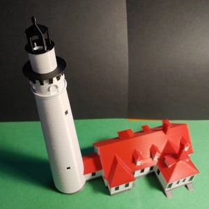 May include: A white lighthouse model with a black roof and a red brick building with a red roof.