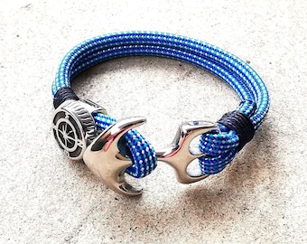 May include: A blue and white rope bracelet with a silver anchor charm. The anchor has a compass design on the top.