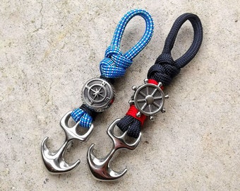 May include: Two keychains with nautical themes. One features a blue and white rope with a compass charm and an anchor. The other features a black and red rope with a ship's wheel charm and an anchor.