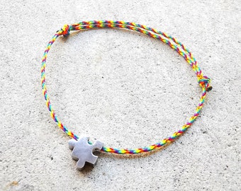May include: A rainbow colored string bracelet with a silver puzzle piece charm.