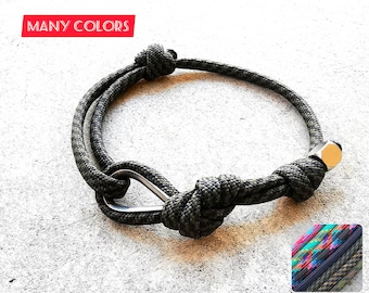 May include: A green paracord bracelet with a silver metal clasp and a silver metal bead. The bracelet is tied with a knot. The text "MANY COLORS" is visible in the top left corner of the image.
