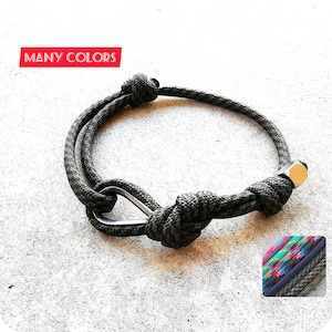 Peut inclure: Un bracelet en paracorde vert avec un fermoir en métal argenté et une perle en métal argenté. Le bracelet est noué. Le texte "MANY COLORS" est visible dans le coin supérieur gauche de l'image.