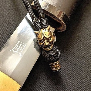 May include: A black sword with a gold-colored hilt and a black cord with a gold-colored oni mask charm. The sword has the kanji for "wind" inscribed on the blade.