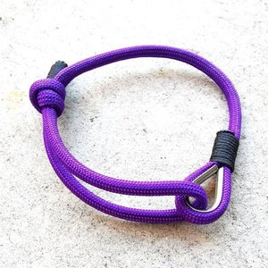 Peut inclure: Un bracelet en cordelette violette avec un fermoir argenté. Le bracelet est noué.