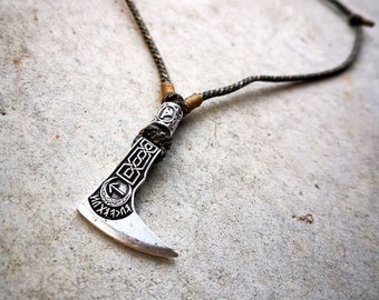May include: A silver axe pendant necklace with a braided cord. The axe has intricate details and runes.