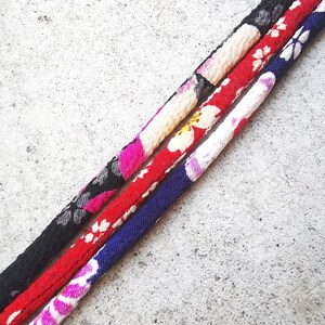 Op de afbeelding: Drie stoffen koorden met bloemenpatronen in zwart, rood en blauw.