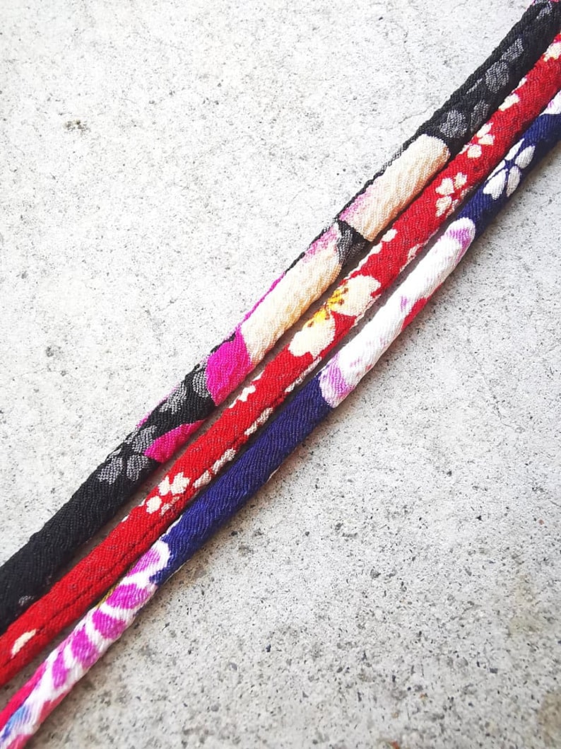 Op de afbeelding: Drie stoffen koorden met bloemenpatronen in zwart, rood en blauw.