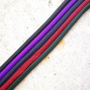 May include: Four different colored ropes, green, red, navy blue, and purple, are laid out in a diagonal line on a white concrete surface.