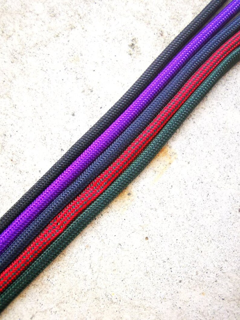 May include: Four different colored ropes, green, red, navy blue, and purple, are laid out in a diagonal line on a white concrete surface.