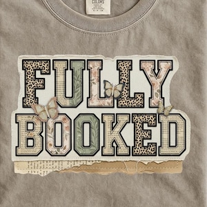 Może przedstawiać: Szara koszulka Comfort Colors z napisem "FULLY BOOKED" w warstwowym wzorze. Litery mają wzory kwiatowe, w cętki i ze stron książek. Motyle są również obecne w projekcie.